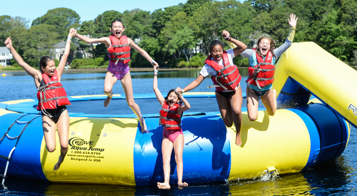Kids holding hands jumping off of the water trampoline into the lake